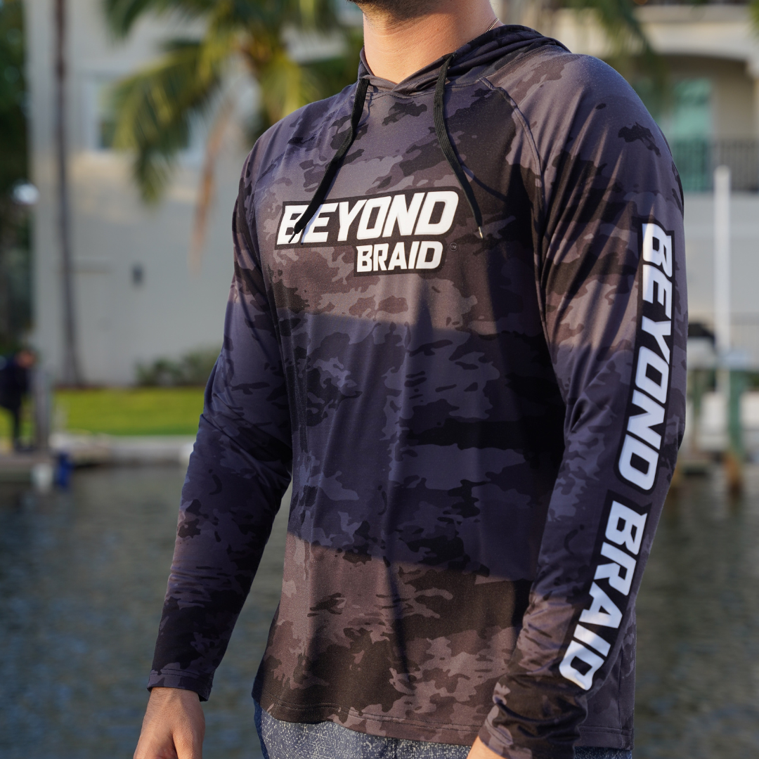 Person wearing a camouflage hoodie with 'BEYOND BRAID' branding outdoors.