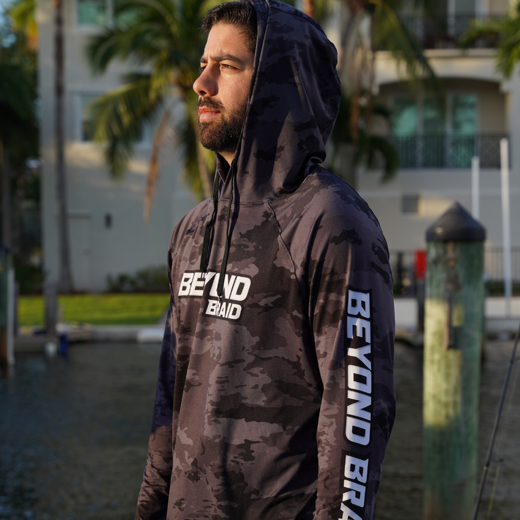 Man wearing a camouflage hoodie with 'BEYOND Braid' branding outdoors.
