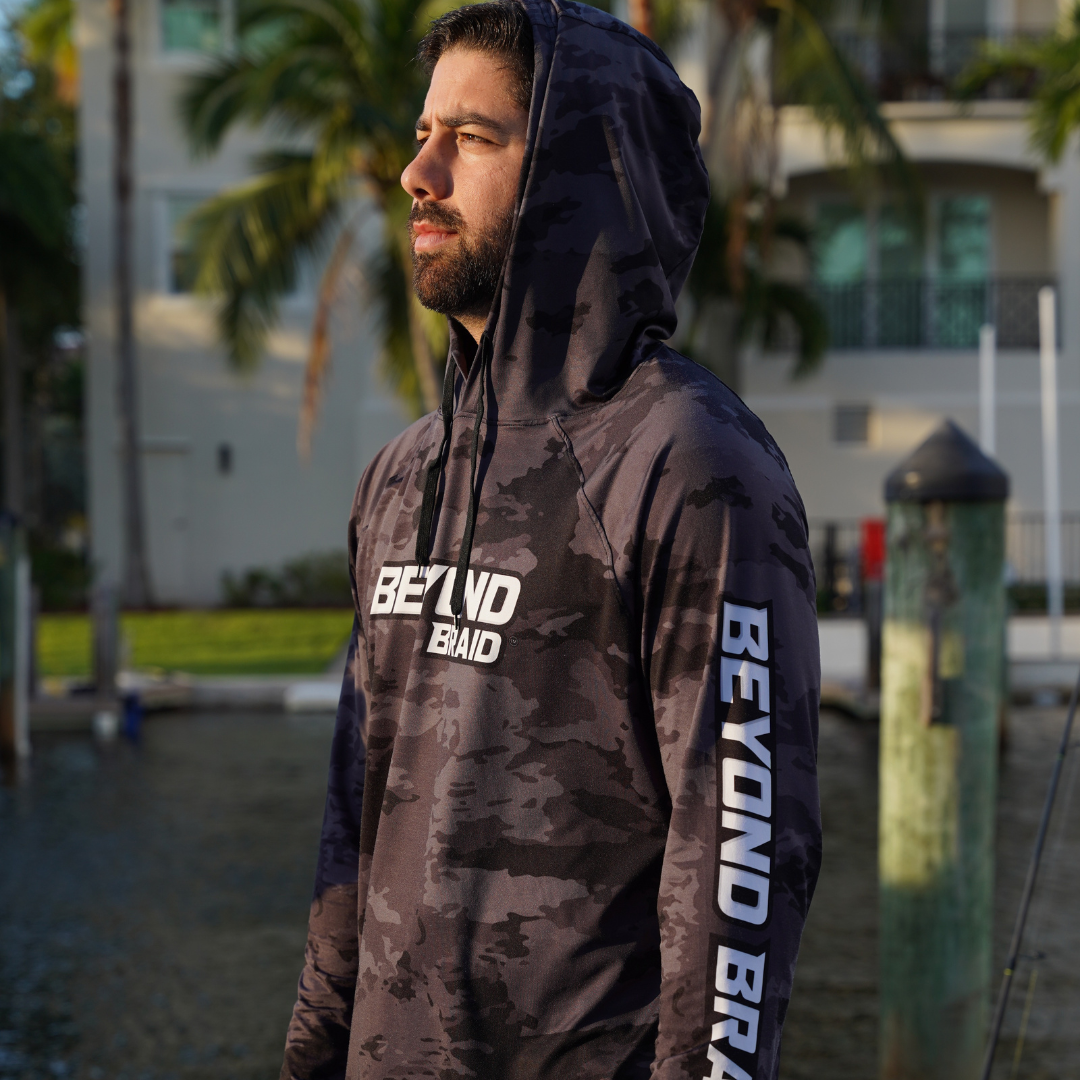 Man wearing a camouflage hoodie with 'BEYOND Braid' branding outdoors.