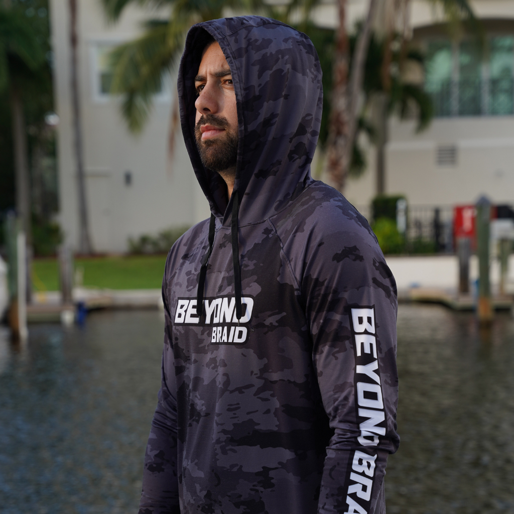 Person wearing a dark camouflage hoodie with 'BEYOND BRAID' branding outdoors.