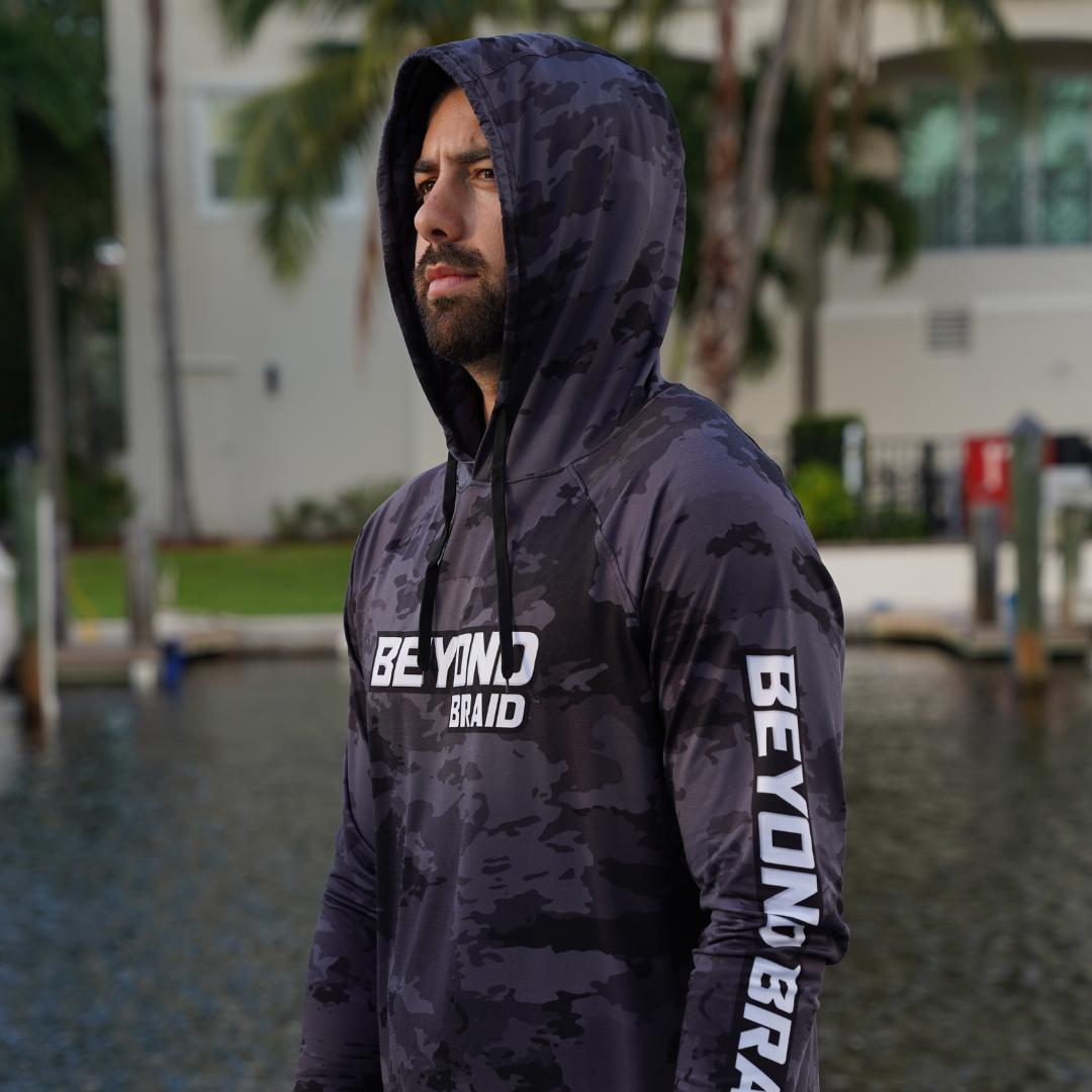 Person wearing a dark camouflage hoodie with 'BEYOND BRAID' branding outdoors.