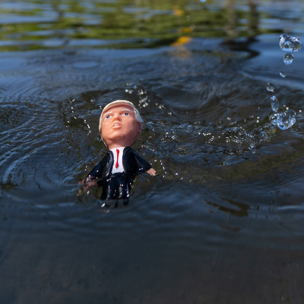 Toy figure of a person in a suit floating in water with ripples around it.