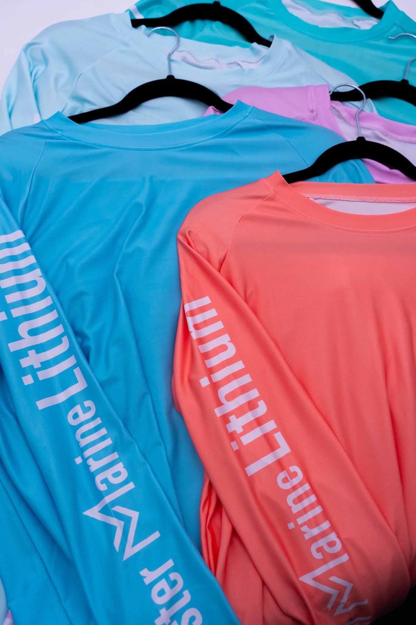 Two long-sleeve shirts in blue and pink with 'Marine Lithium' branding on hangers.