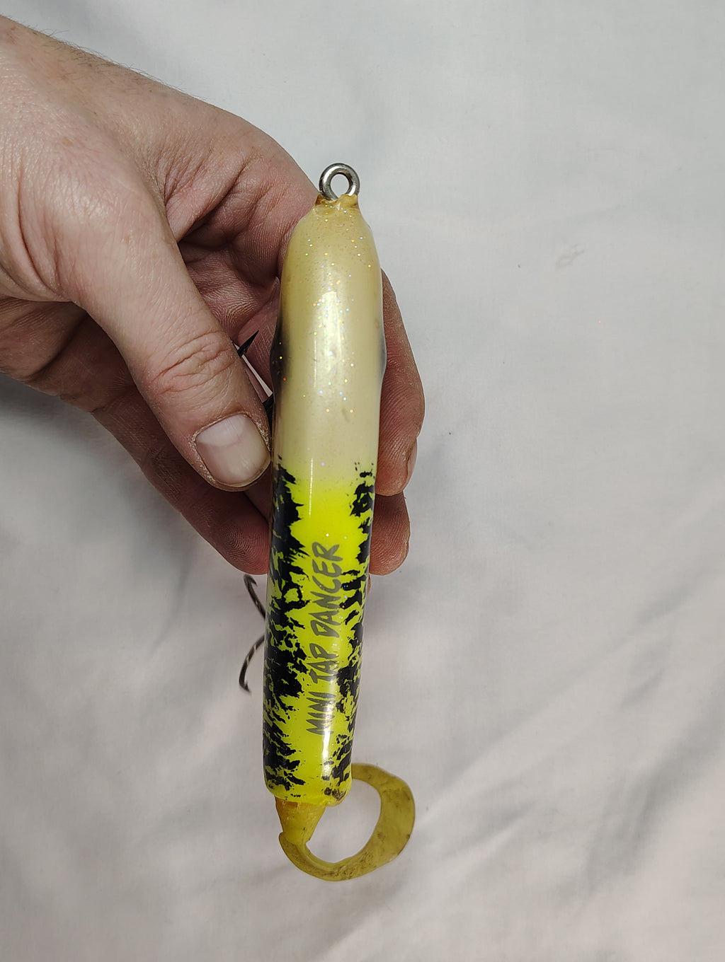 Hand holding a yellow and black fishing lure against a plain background