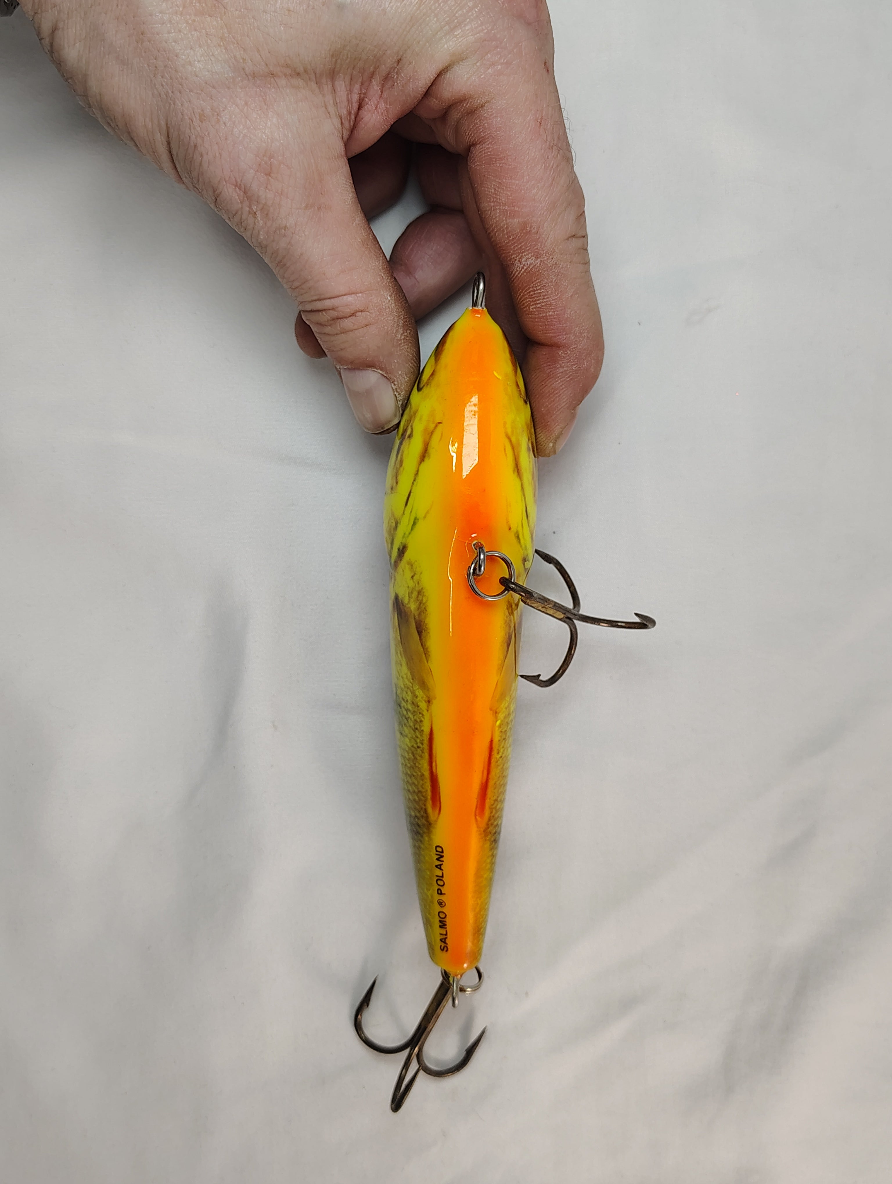 Hand holding a yellow and orange fishing lure against a plain background