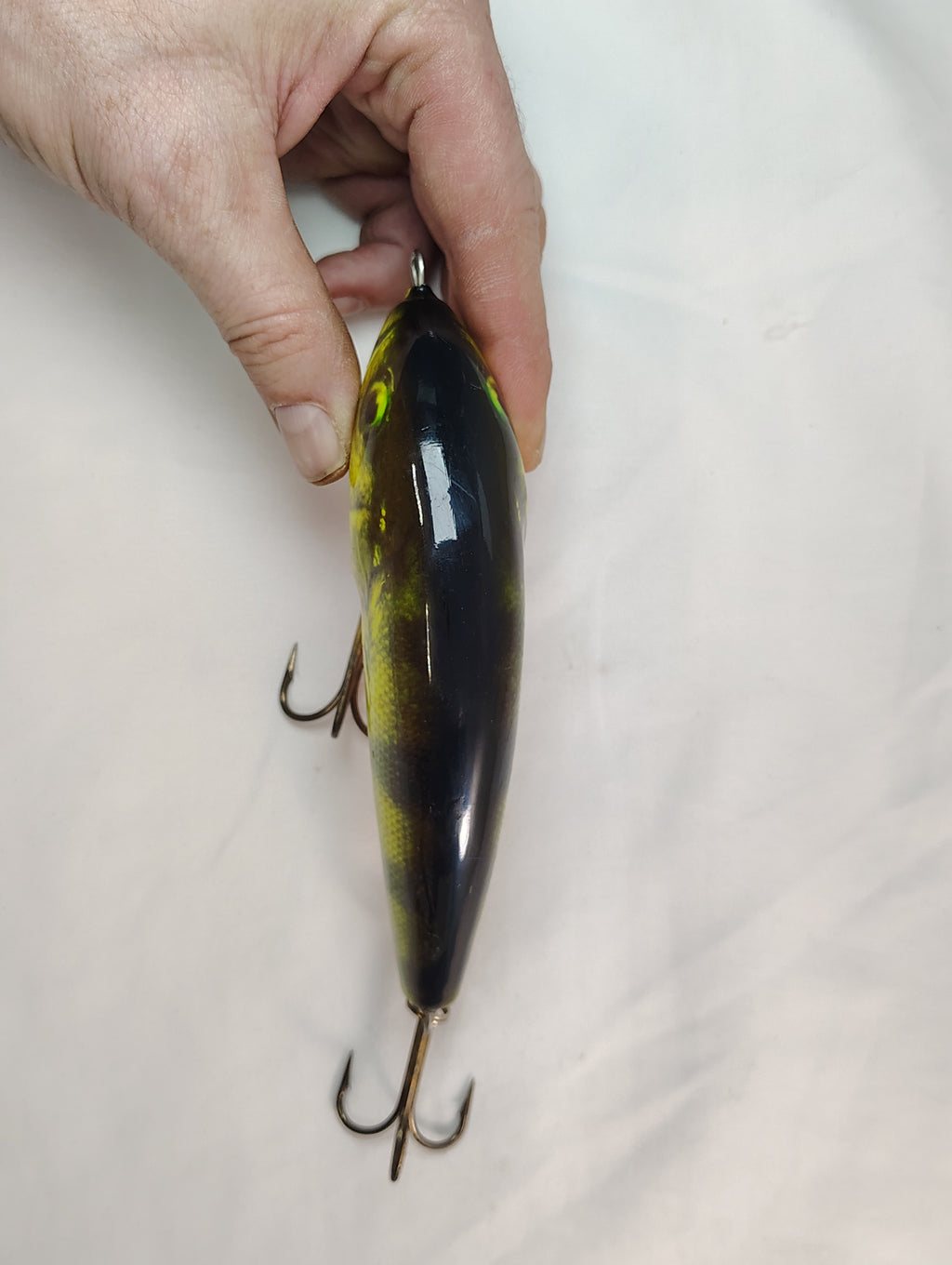 Hand holding a black and yellow fishing lure against a white background