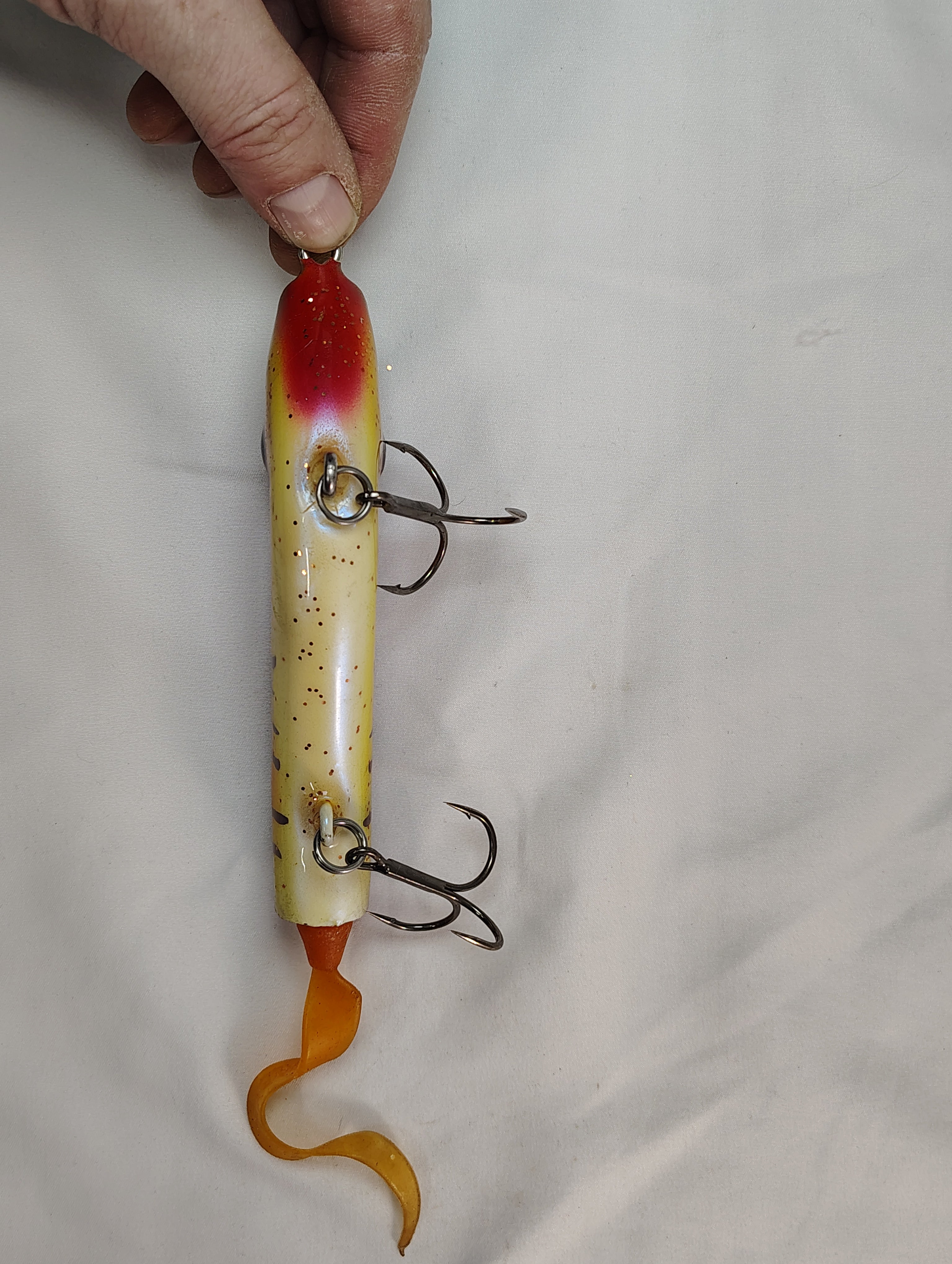 Fishing lure with multiple hooks held by a hand on a light gray background