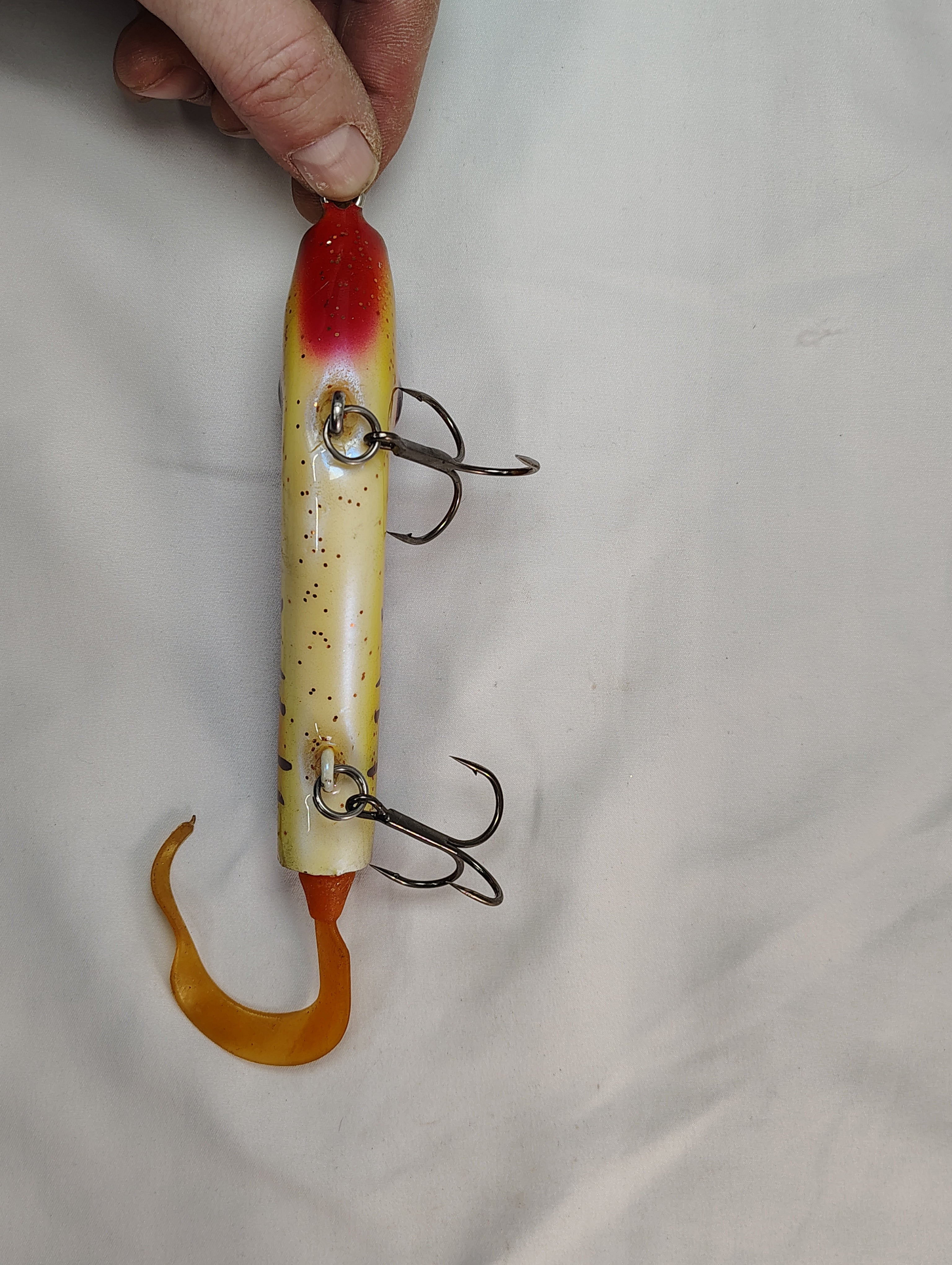 Fishing lure with multiple hooks held by a hand on a light gray background