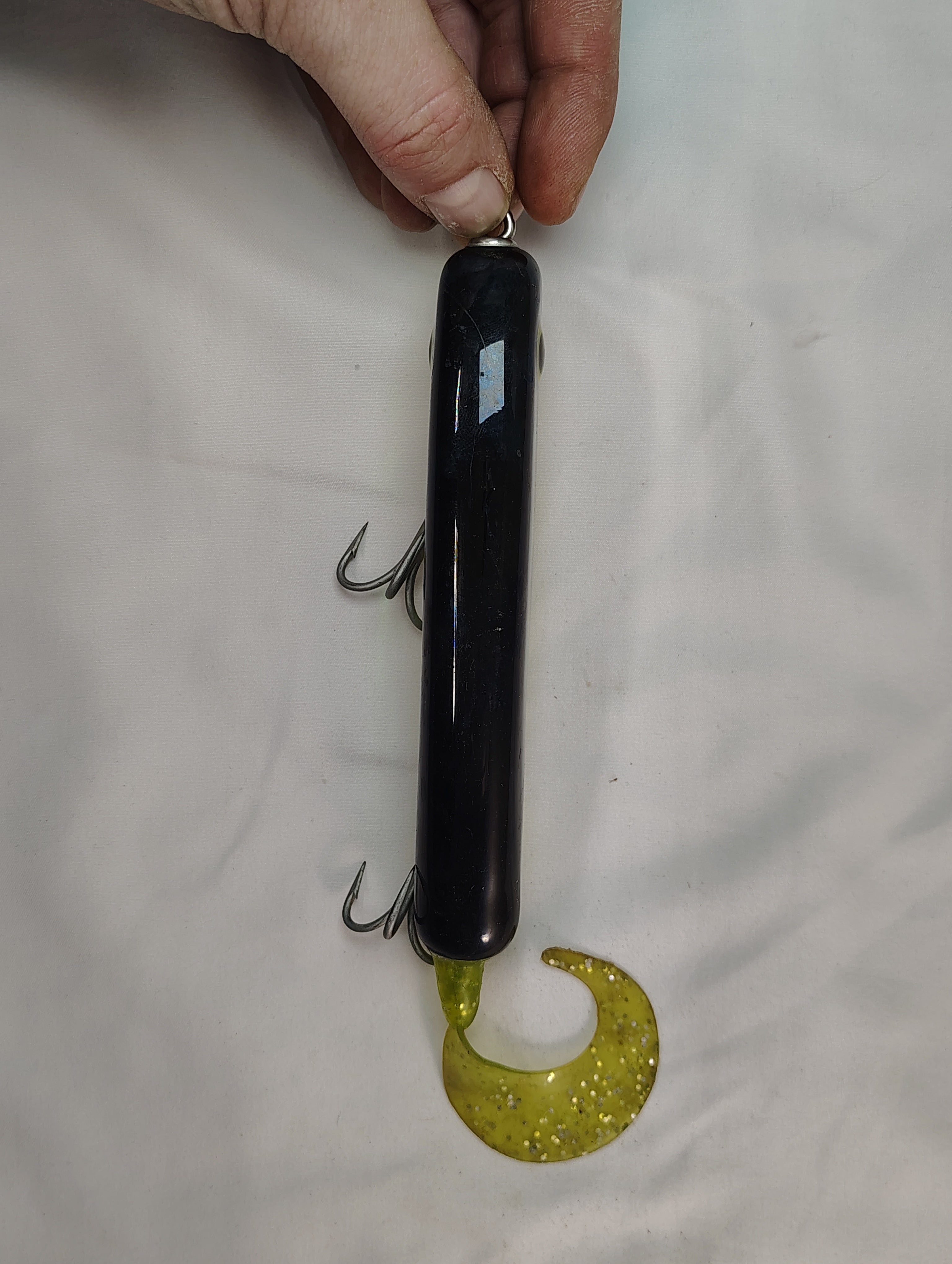 Fishing lure with a black body and yellow treble hook on a white background
