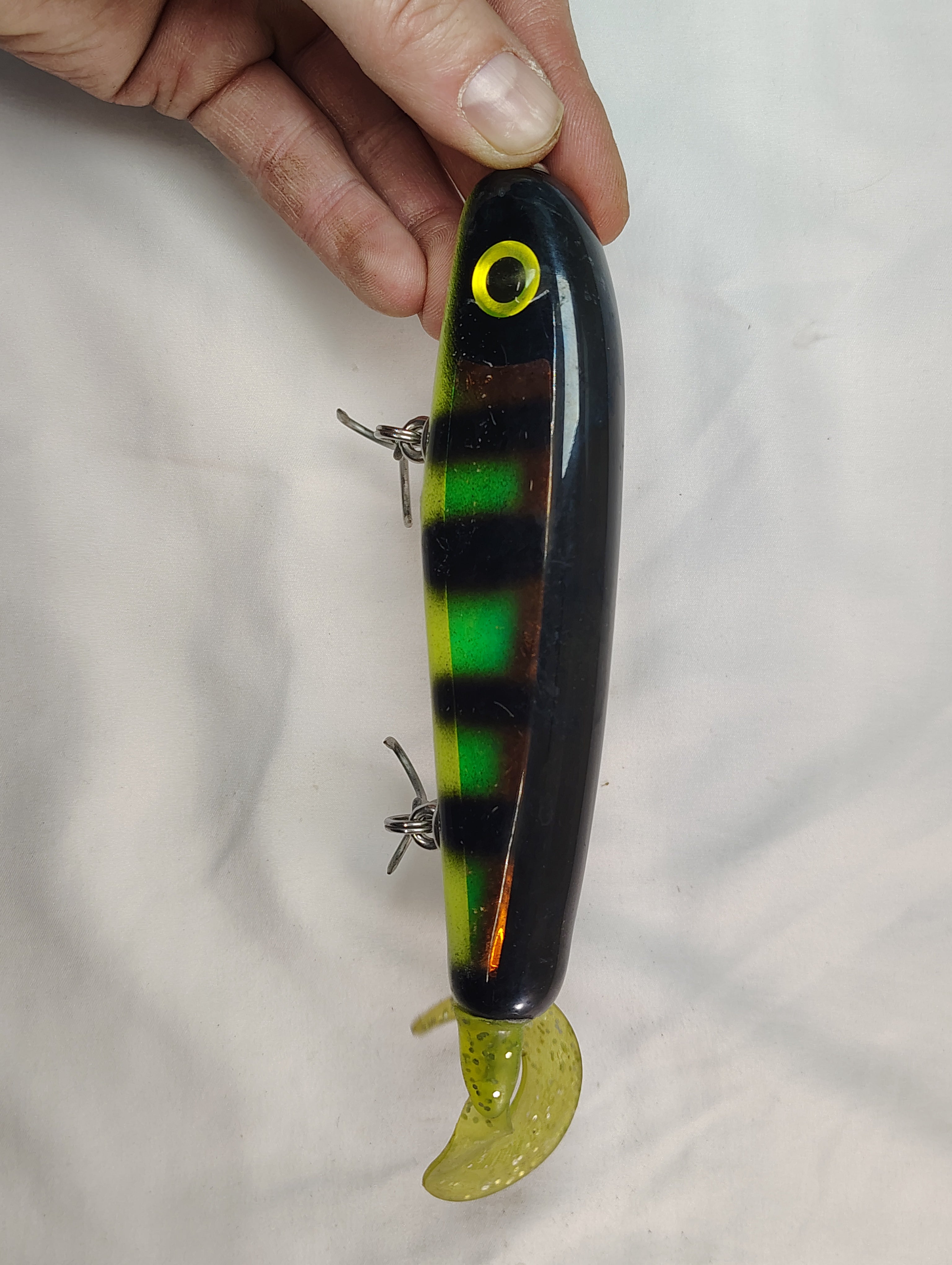 Fishing lure with striped body and green tail held by a hand against a white background