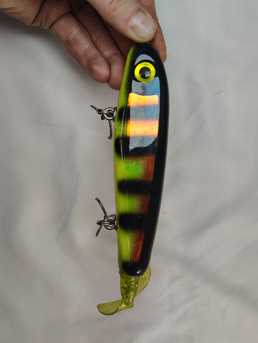Fishing lure with striped pattern held by a hand against a plain background
