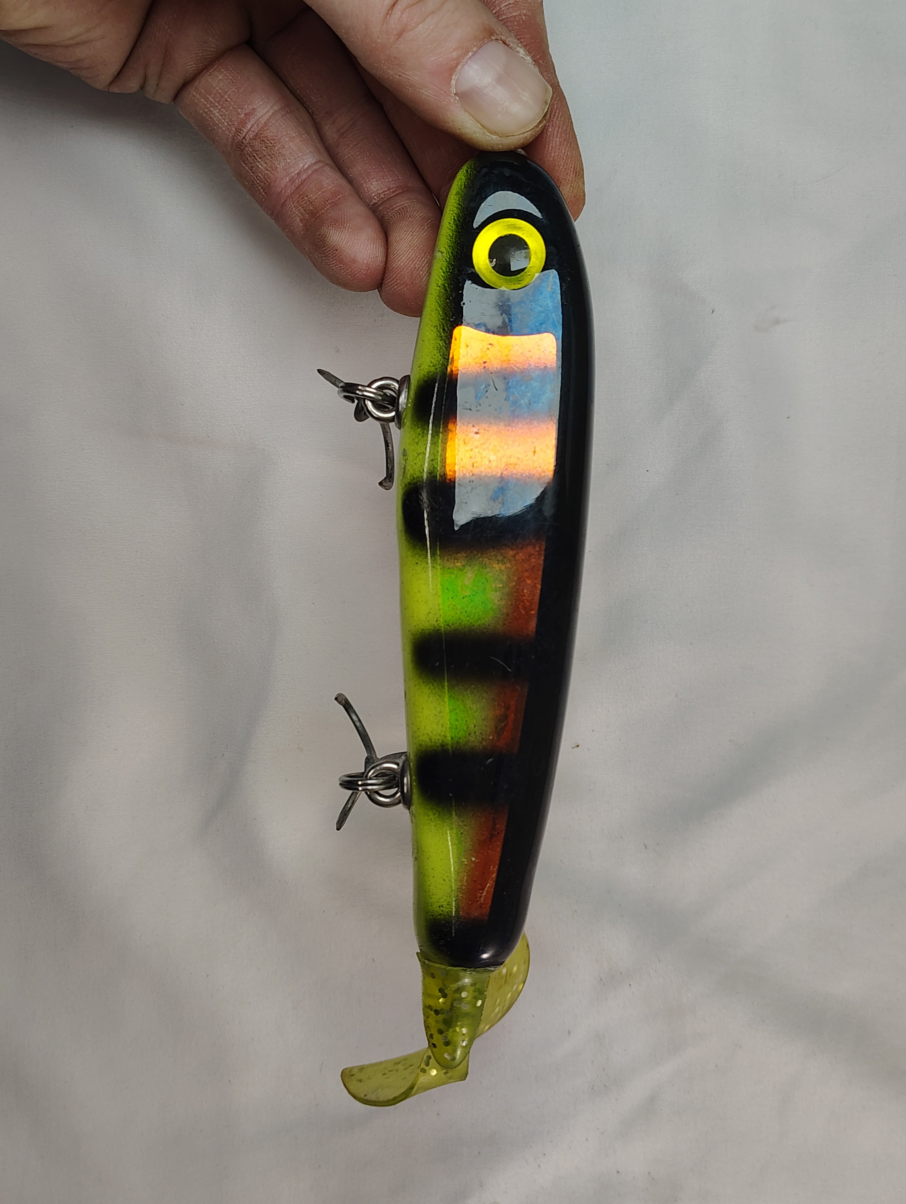 Fishing lure with striped pattern held by a hand against a plain background