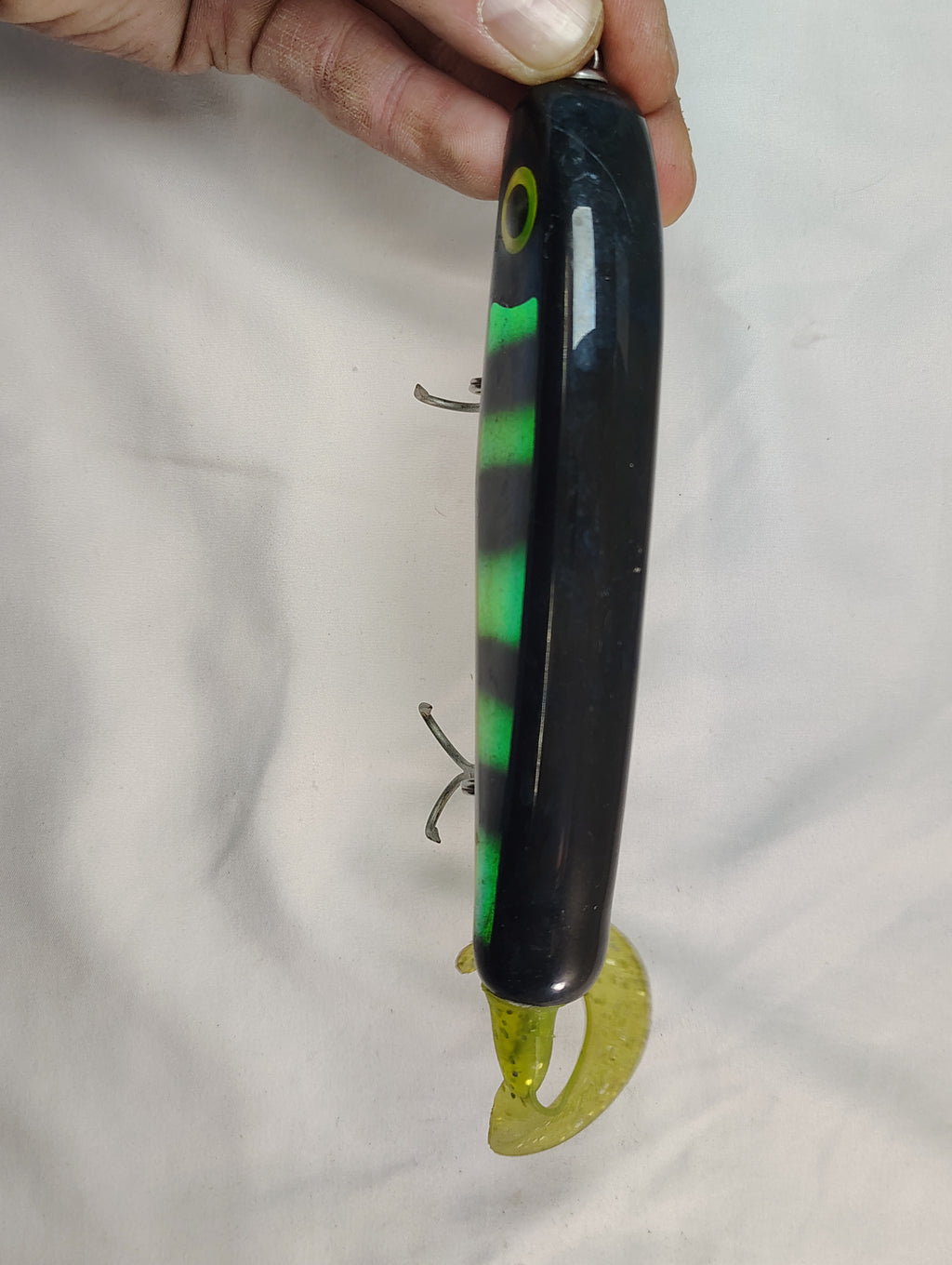 Fishing lure with black and green body held by a hand against a white background