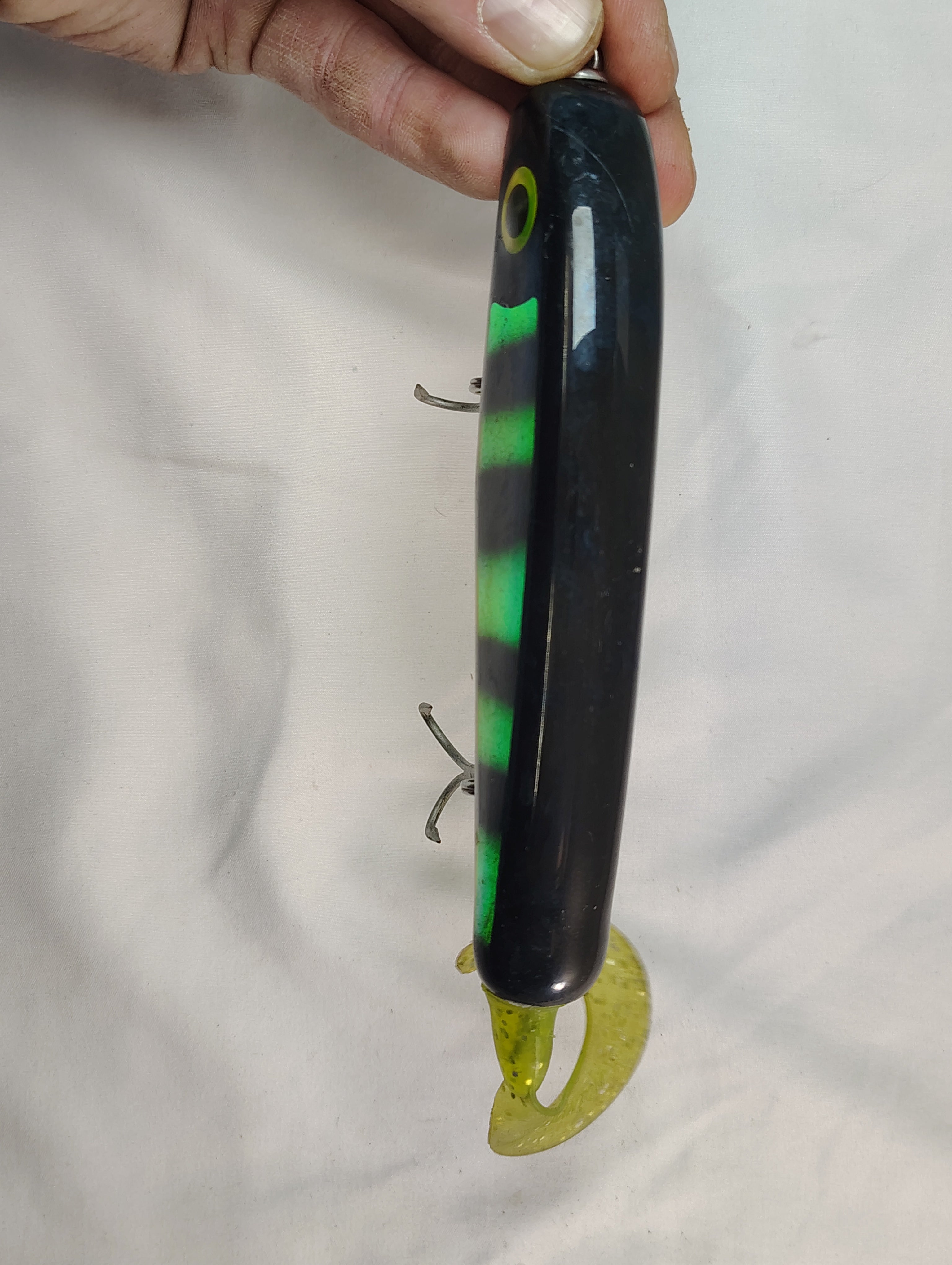 Fishing lure with black and green body held by a hand against a white background