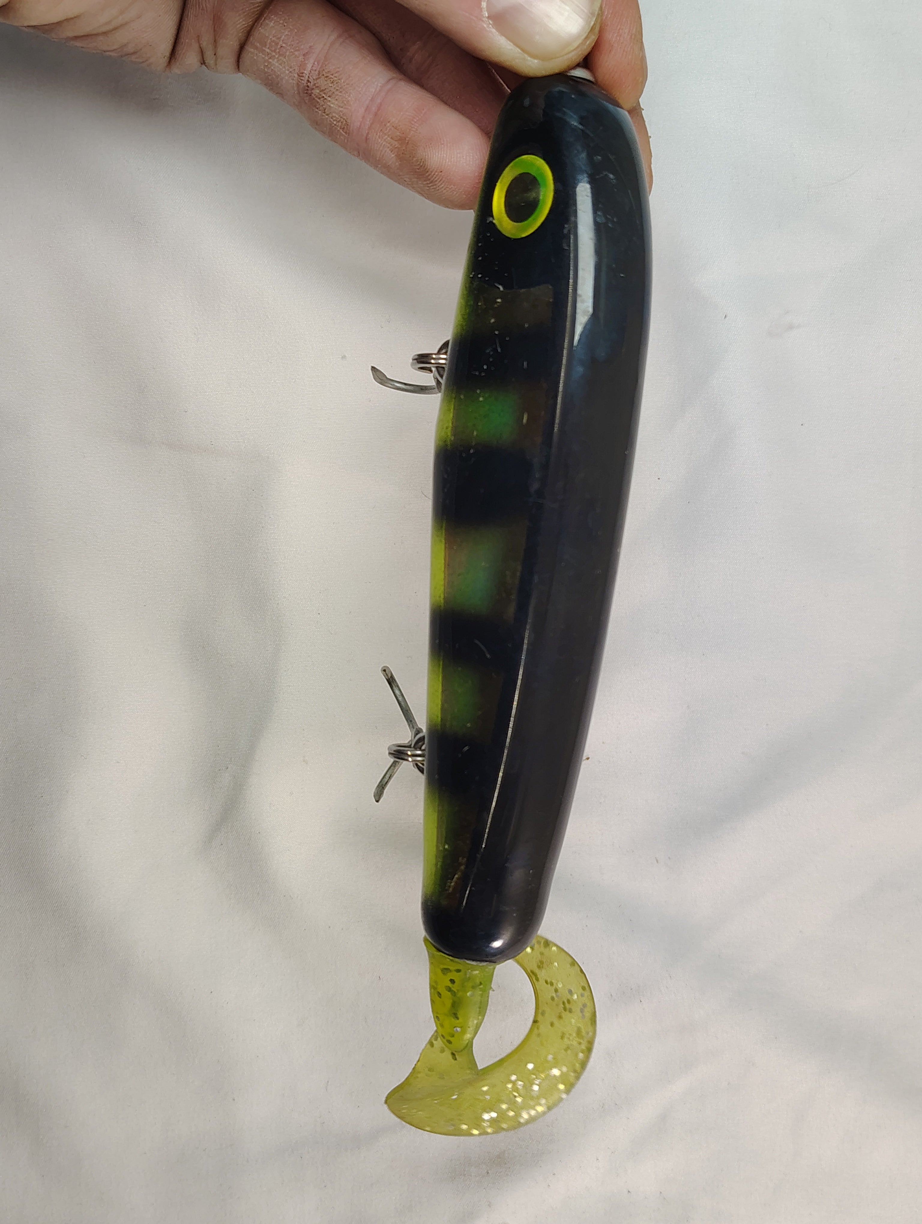 Black and green fishing lure held by a hand against a white background