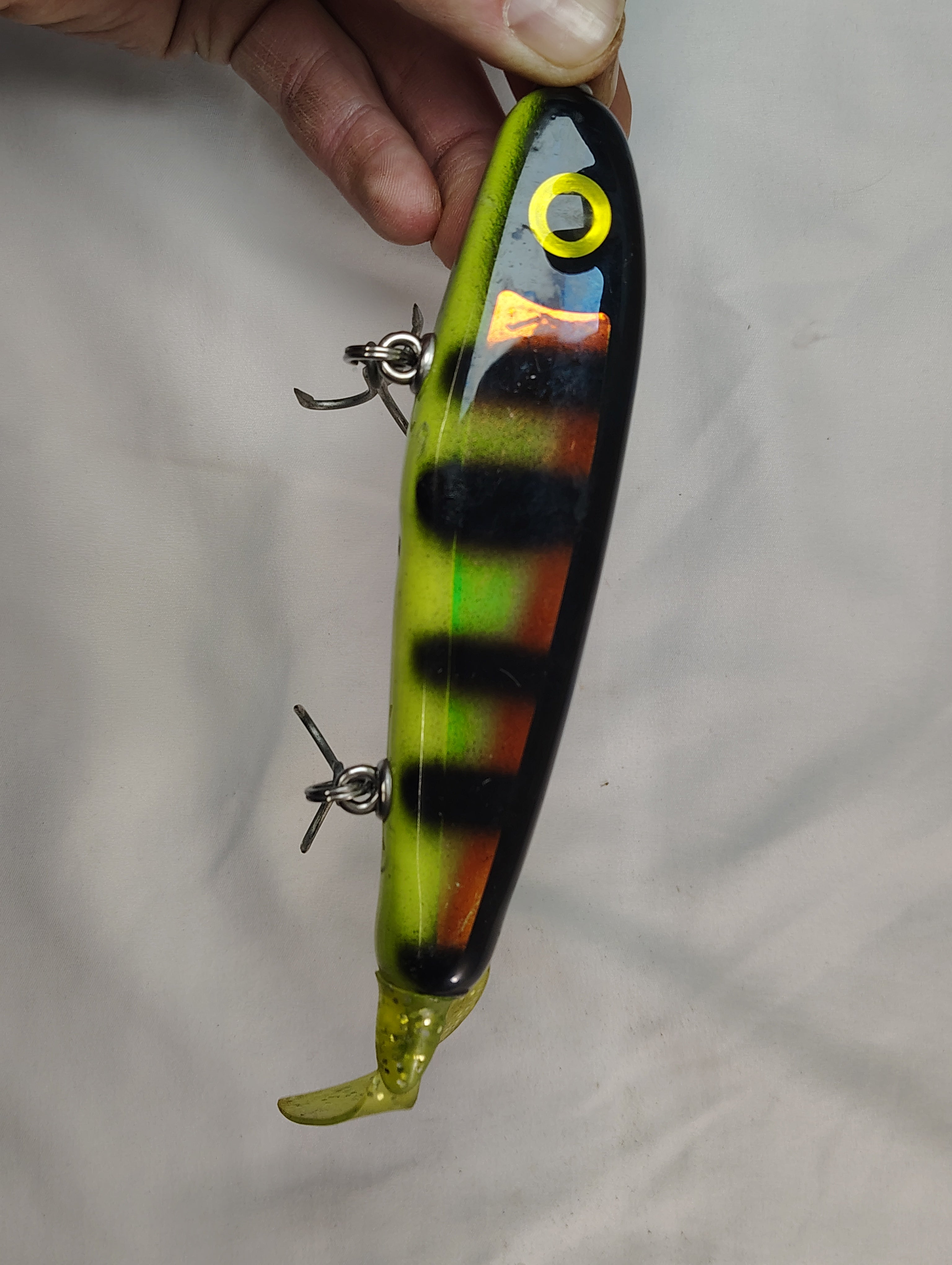 Colorful fishing lure held by a hand against a plain background