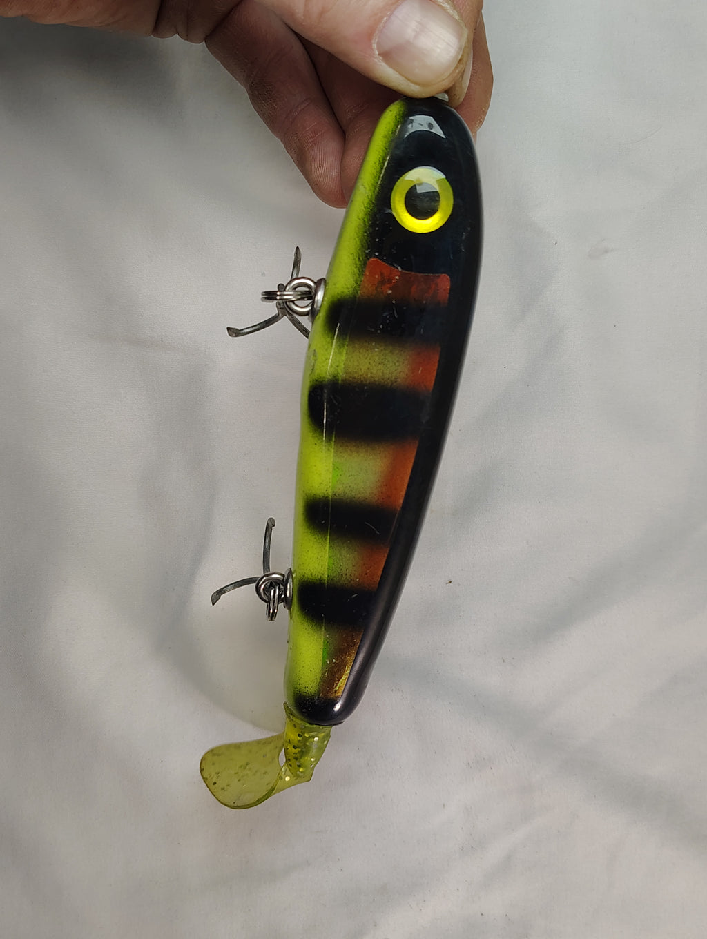 Fishing lure with a striped pattern held by a hand against a plain background