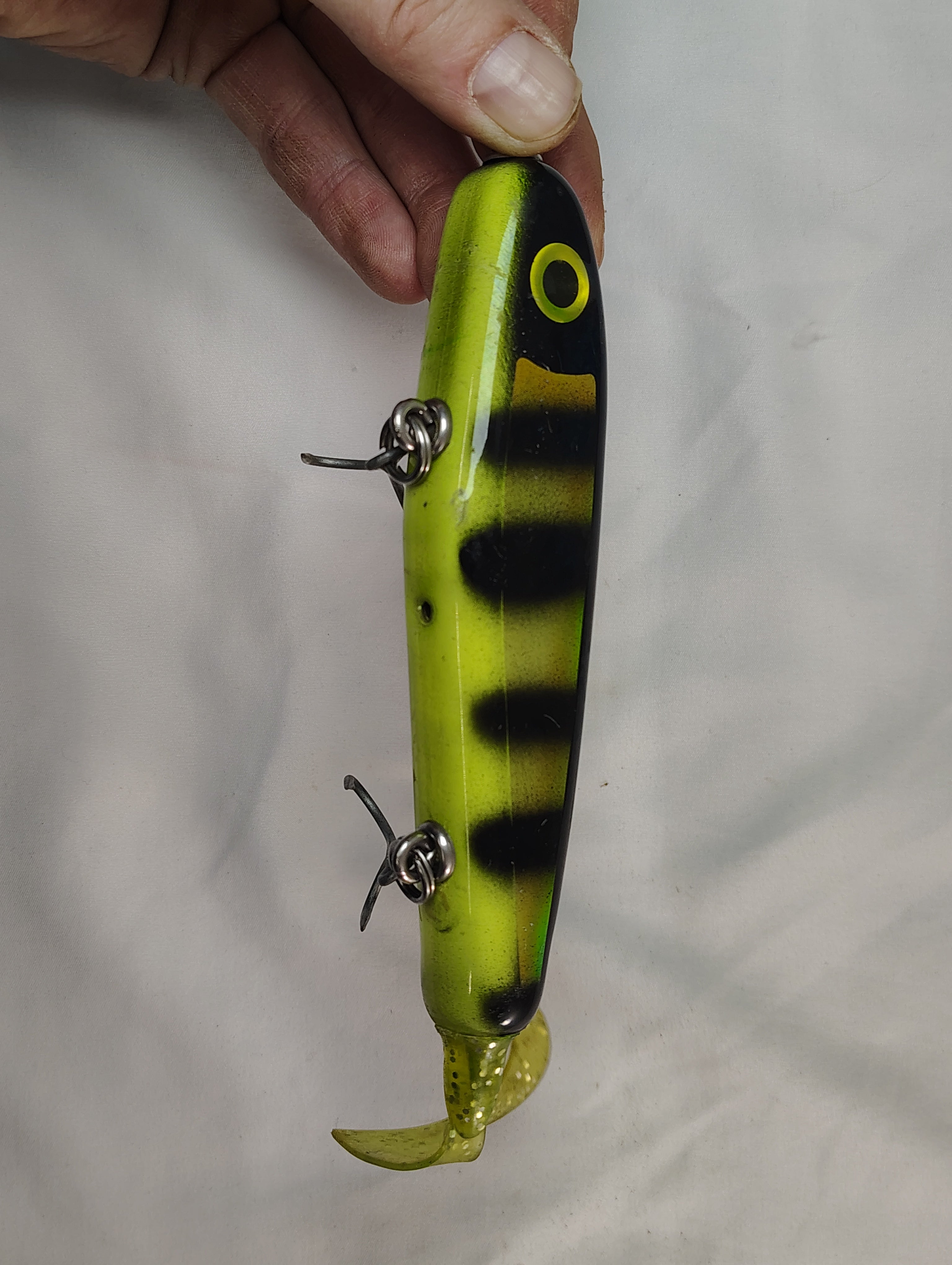 Yellow and black striped fishing lure held by a hand against a plain background