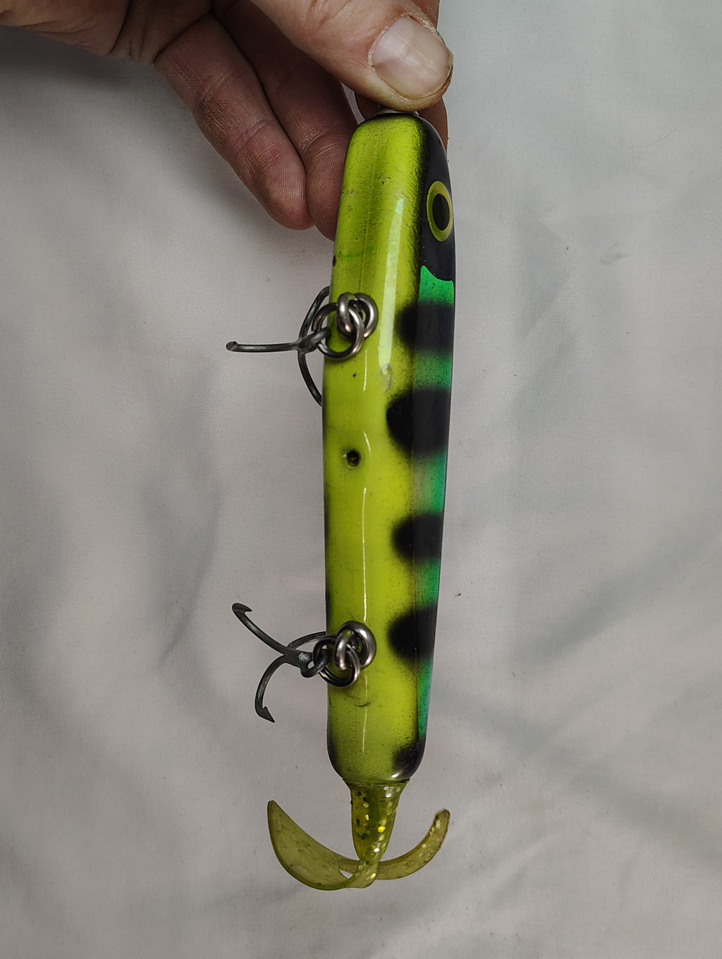 Fishing lure with a striped pattern held by a hand against a plain background