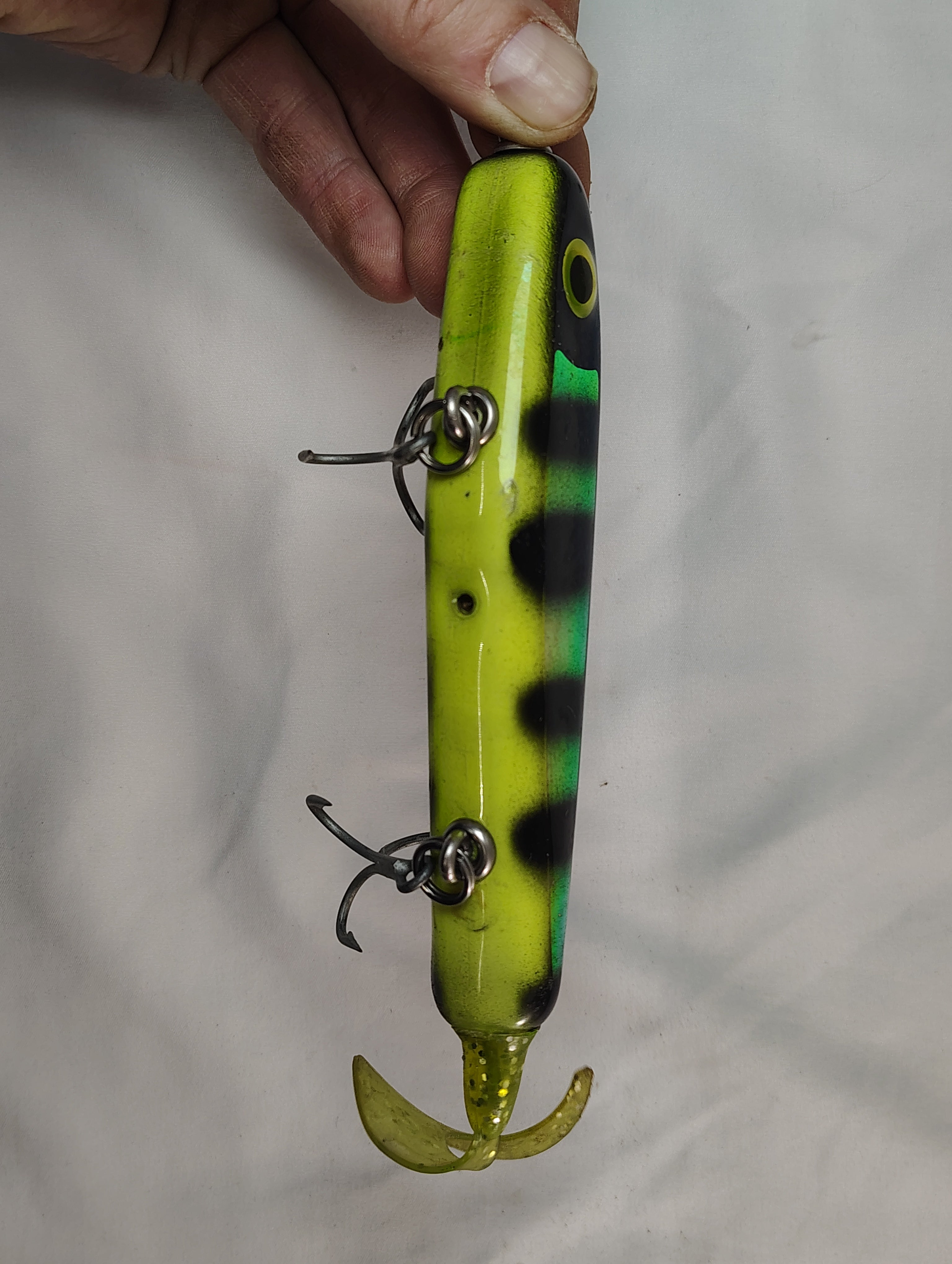 Fishing lure with a striped pattern held by a hand against a plain background