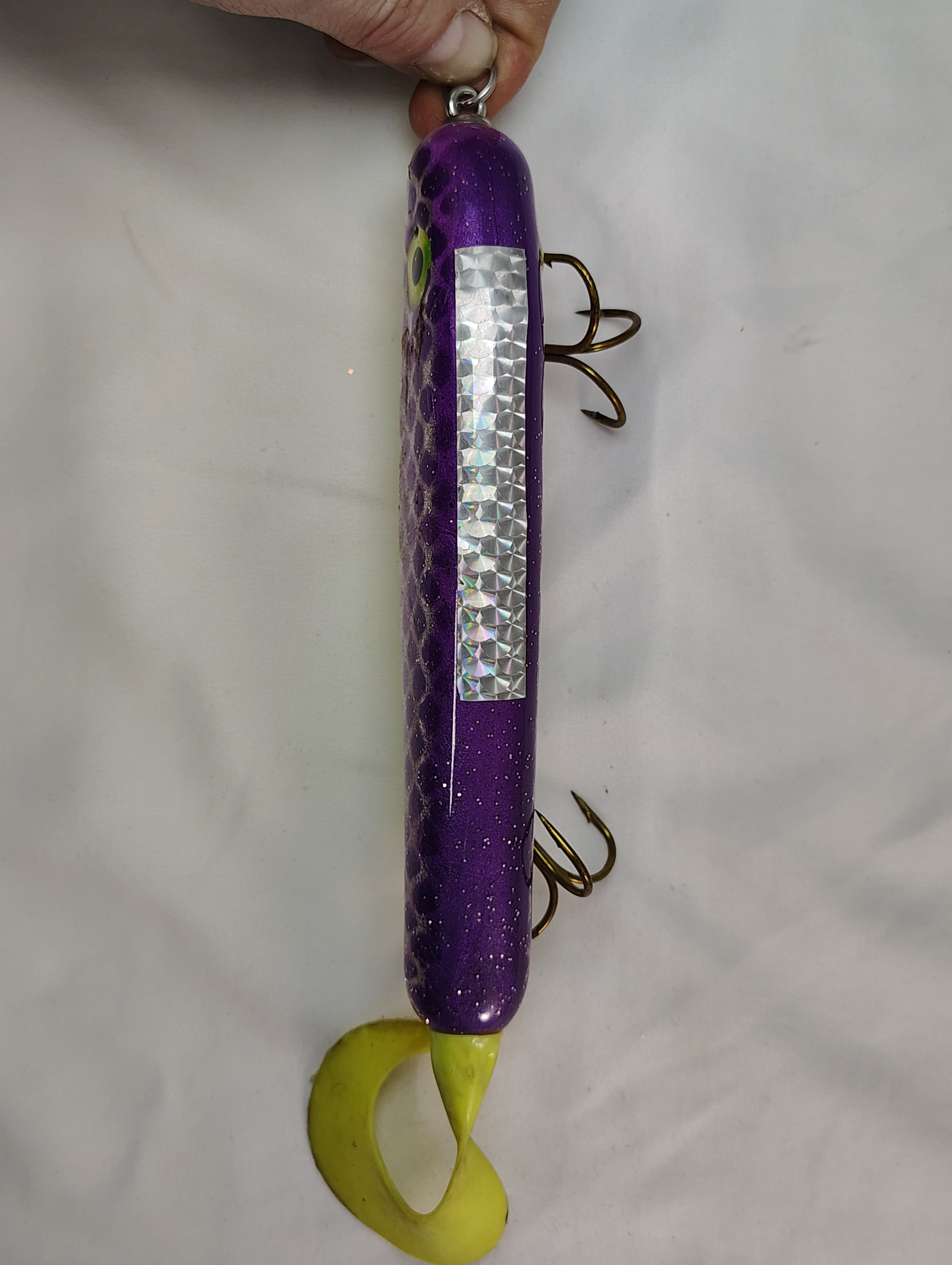 Purple and green fishing lure held by a hand on a white background