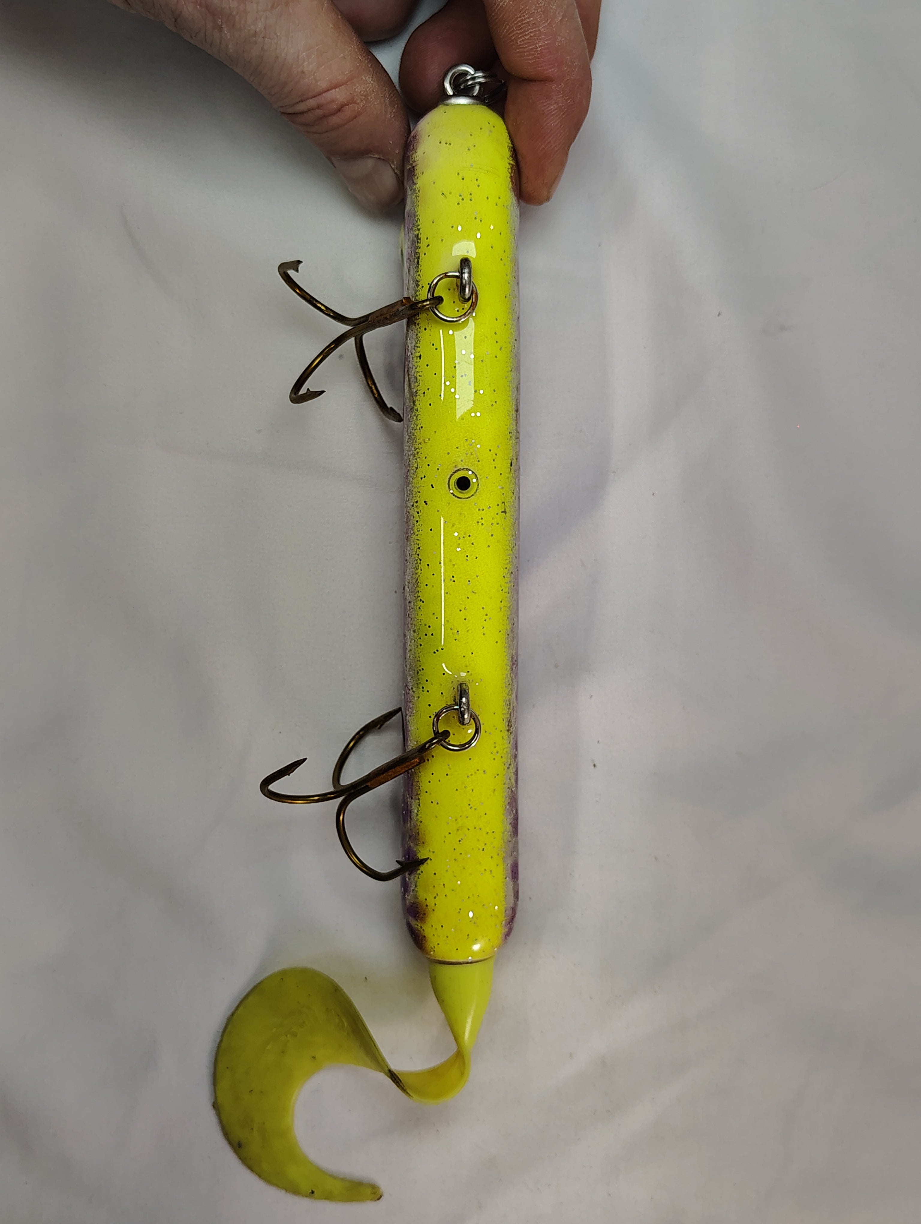 Yellow fishing lure with treble hooks held by a hand on a white background