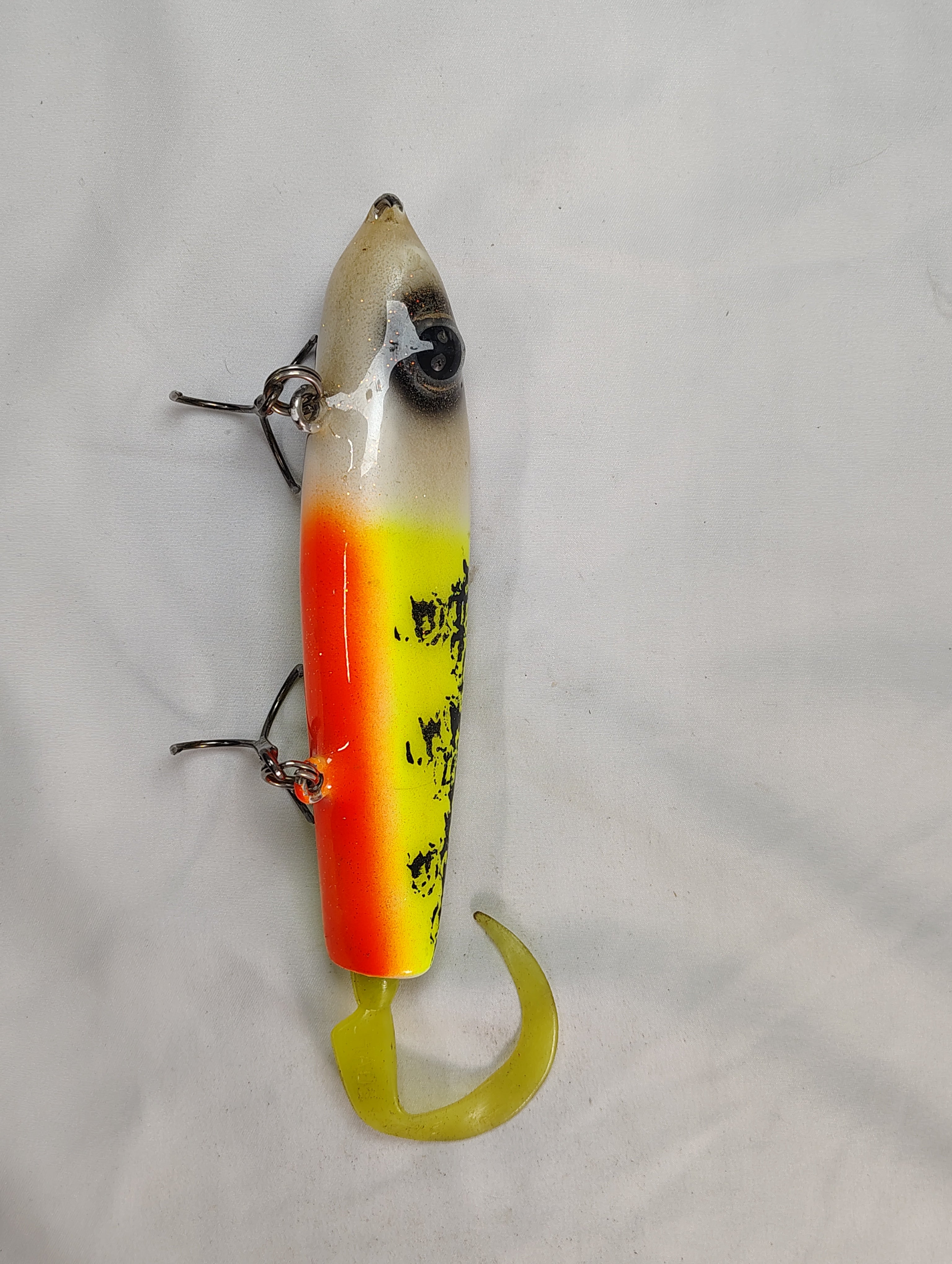 Fishing lure with a white, orange, and yellow body on a gray background