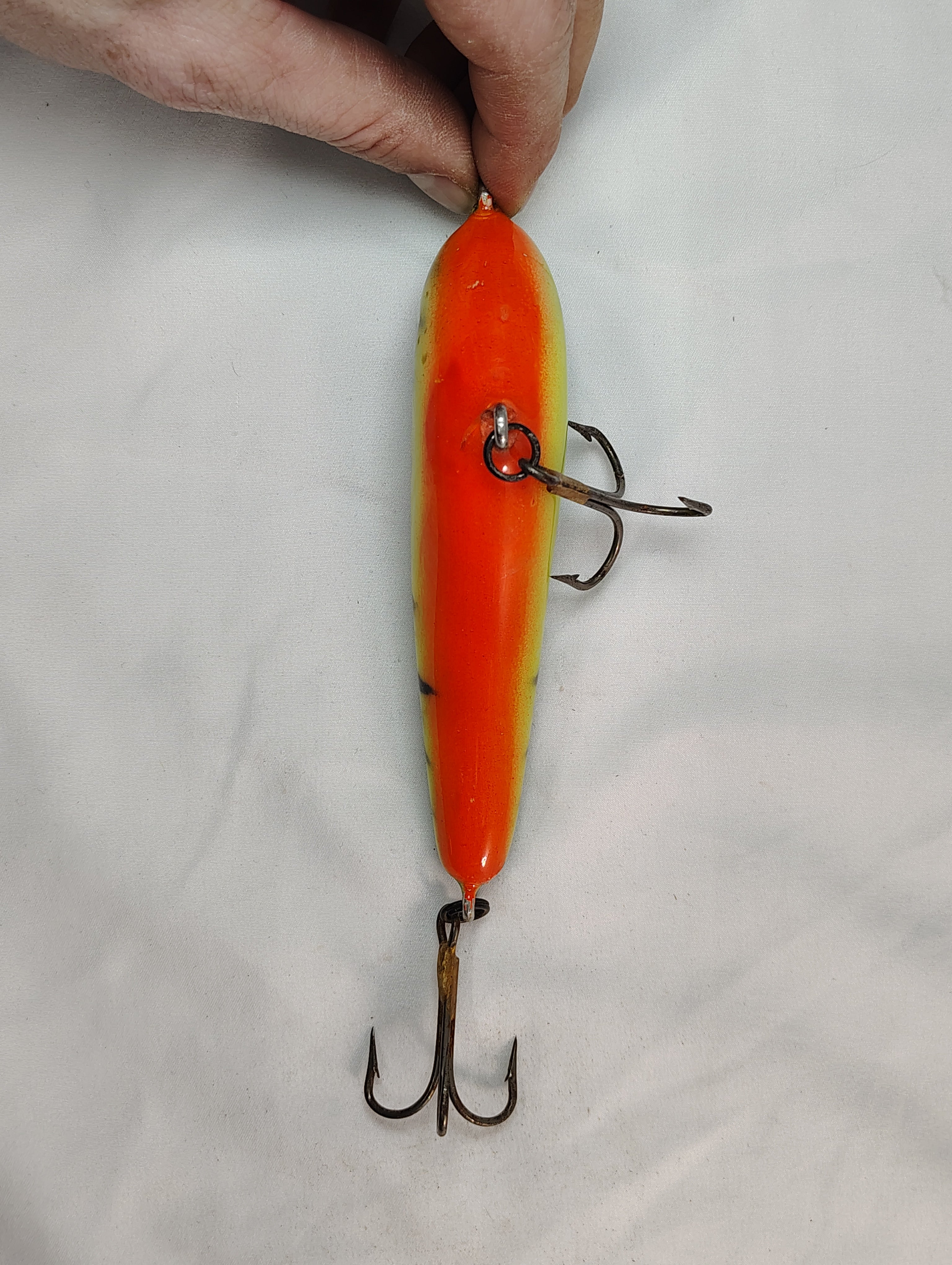 Orange and yellow fishing lure with treble hooks on a white background