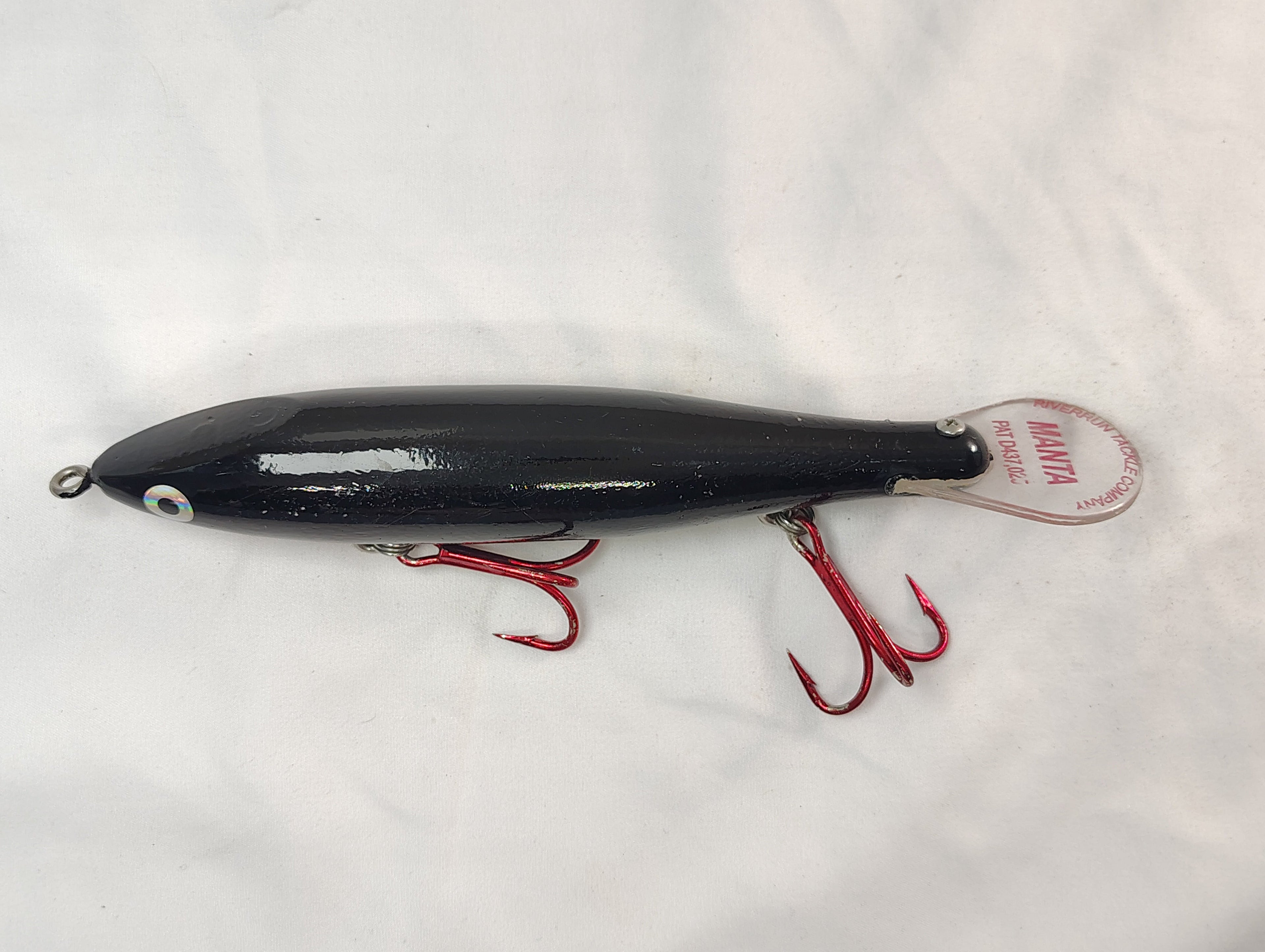 Black fishing lure with red hooks on a white background