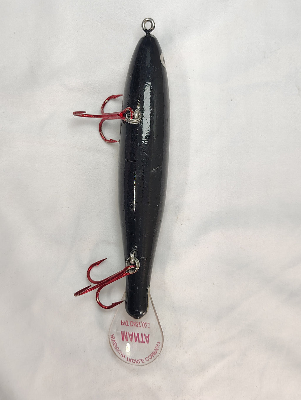 Black fishing lure with red hooks on a white background