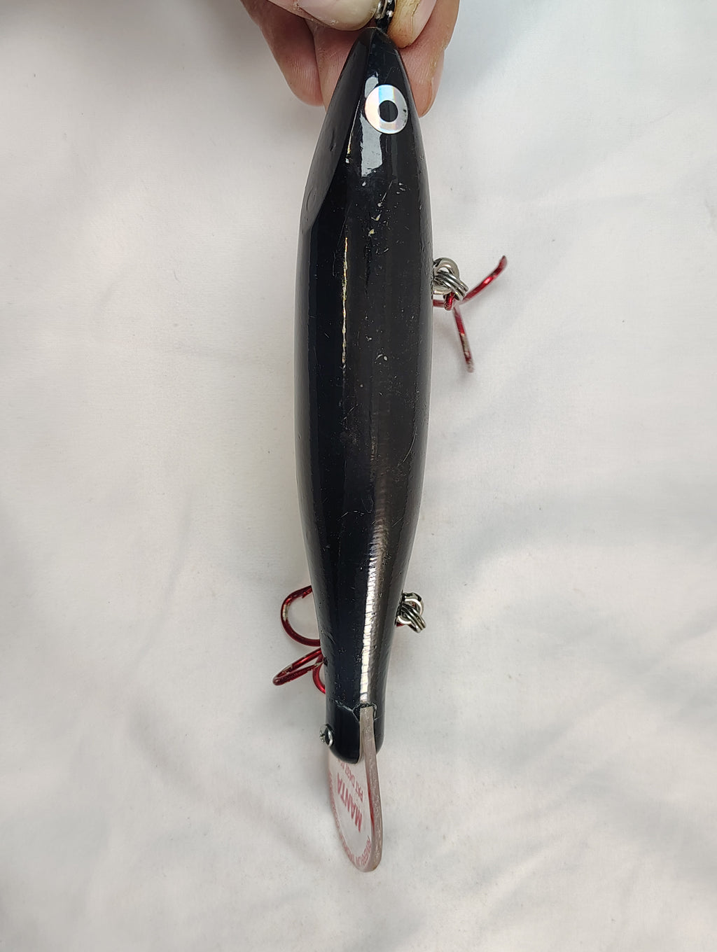 Black fishing lure held by a hand on a white background