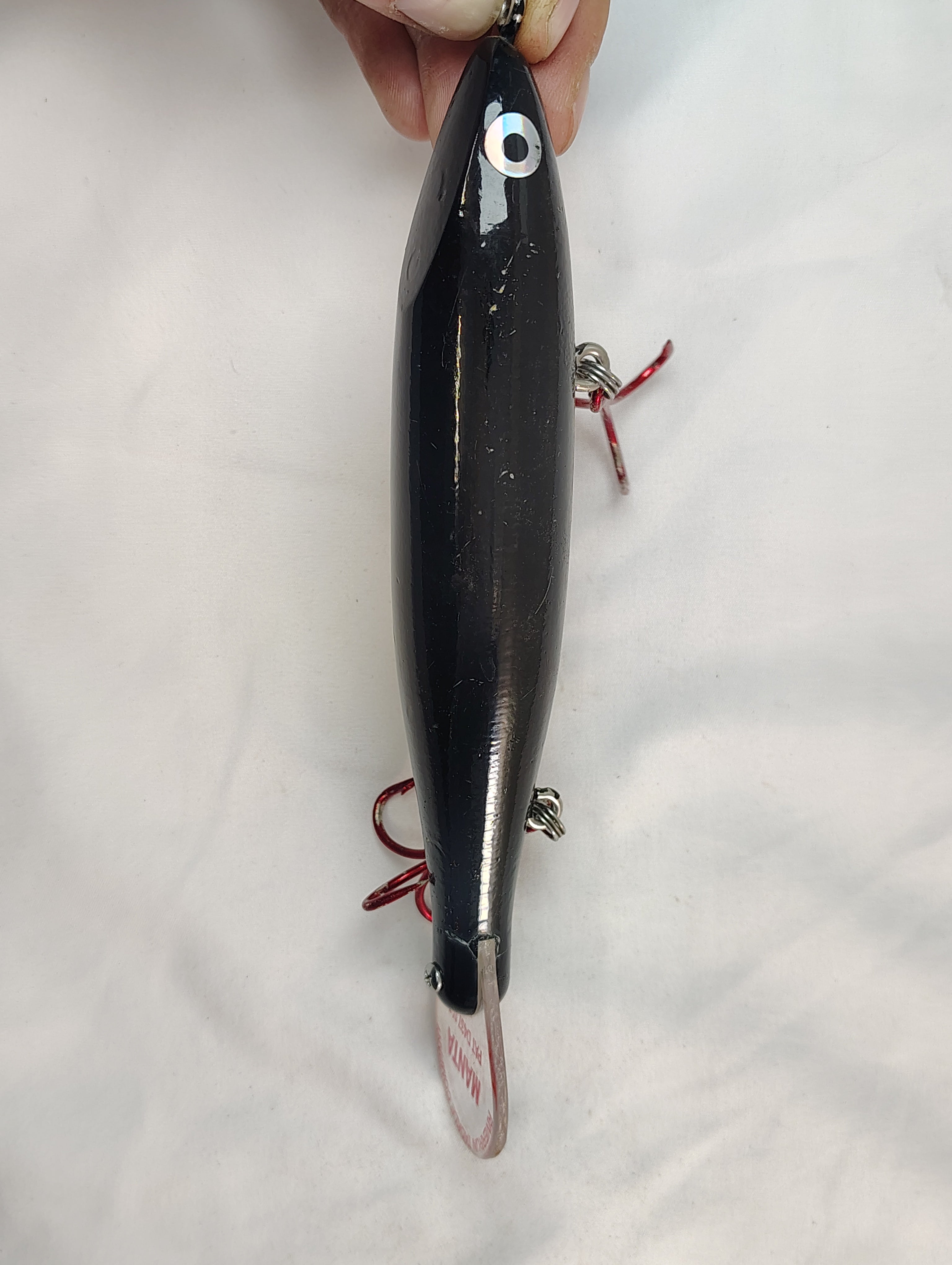 Black fishing lure held by a hand on a white background