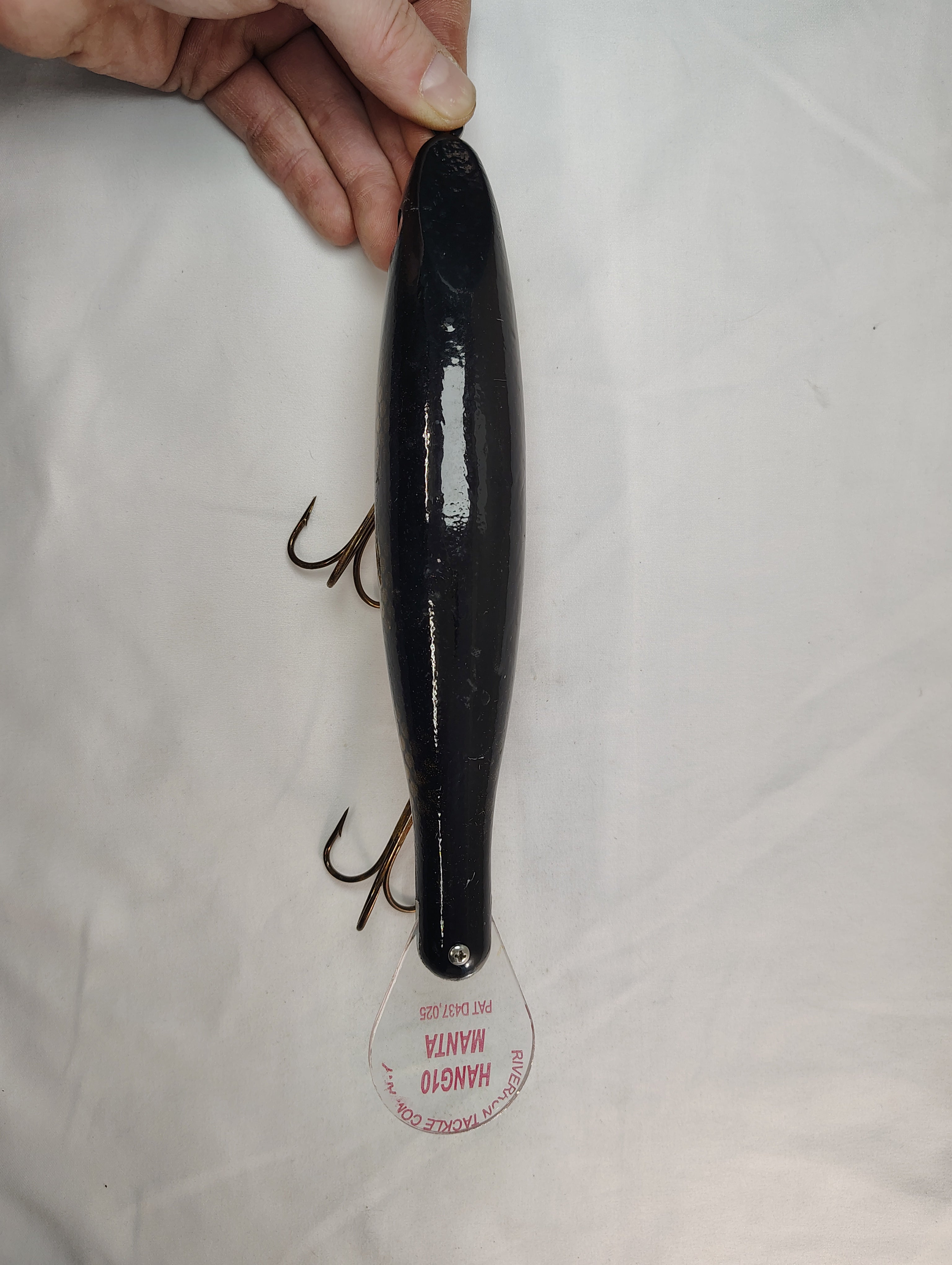 Black fishing lure held by a hand on a white background