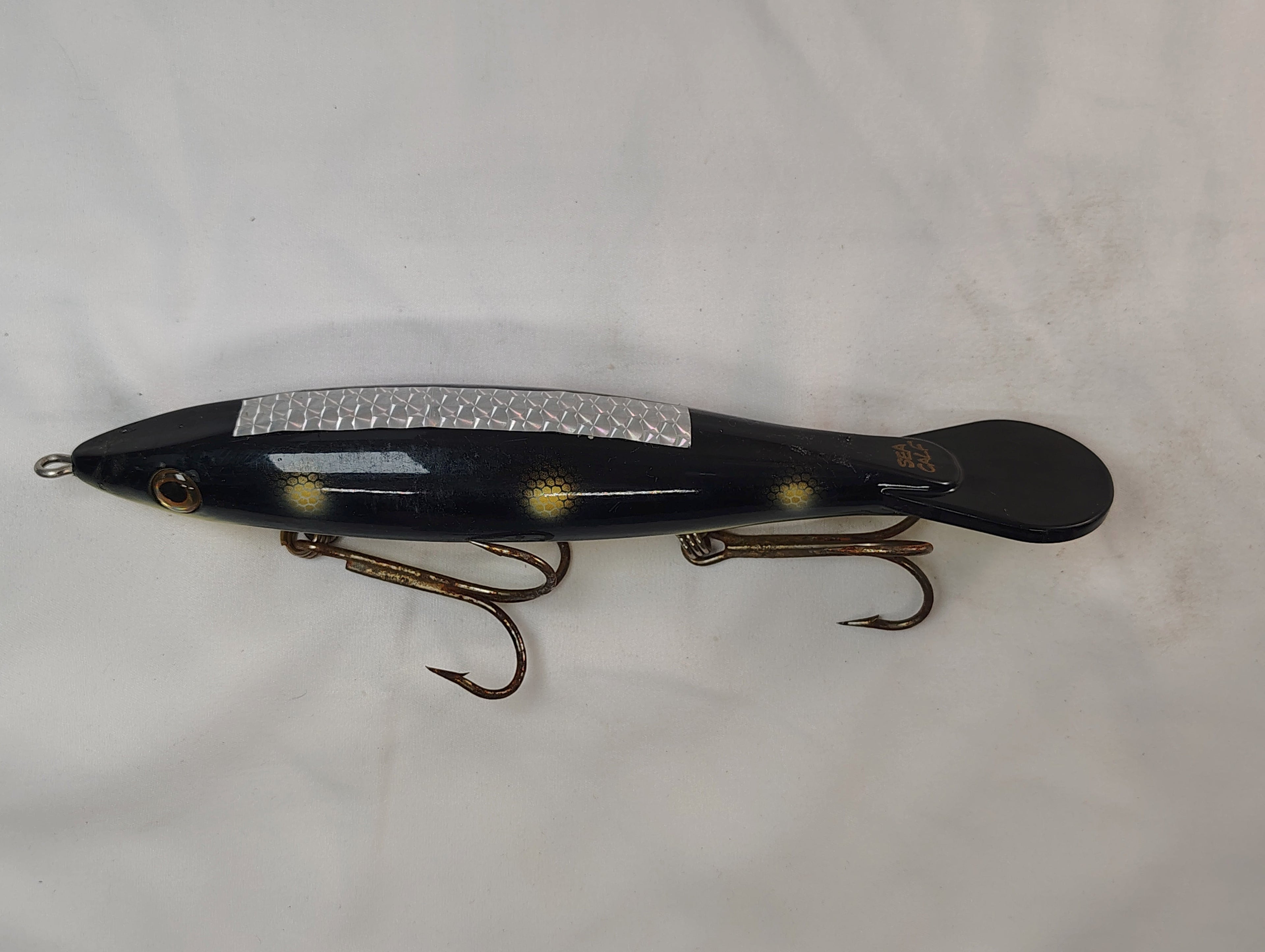 Fishing lure with a metallic body and treble hooks on a white background