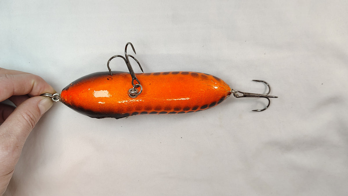 Orange fishing lure held by a hand on a white background