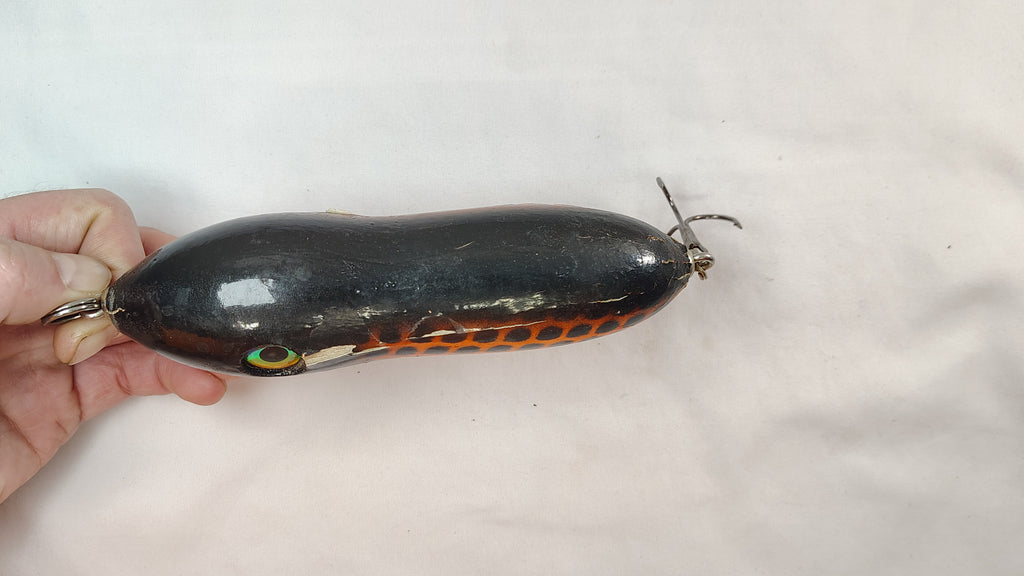 Black and orange fishing lure held by a hand on a white background