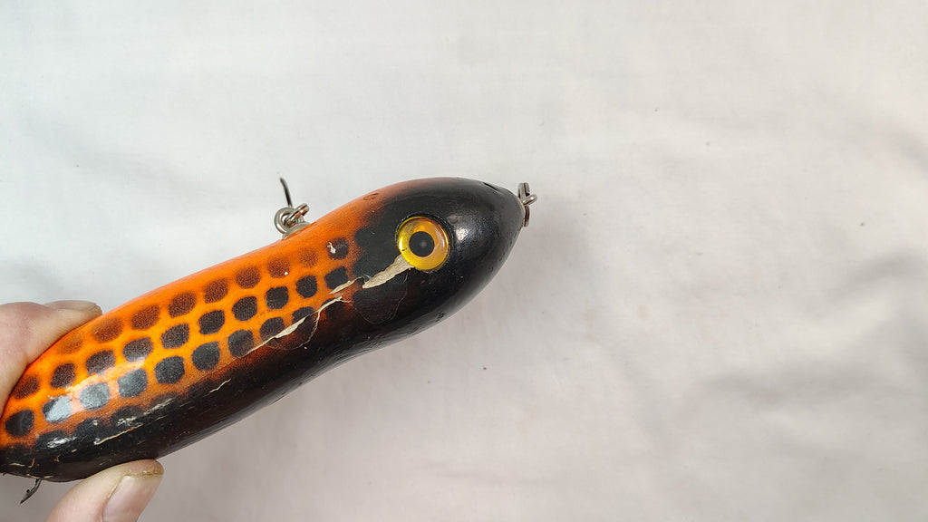 Orange and black fishing lure held by a hand on a light gray background