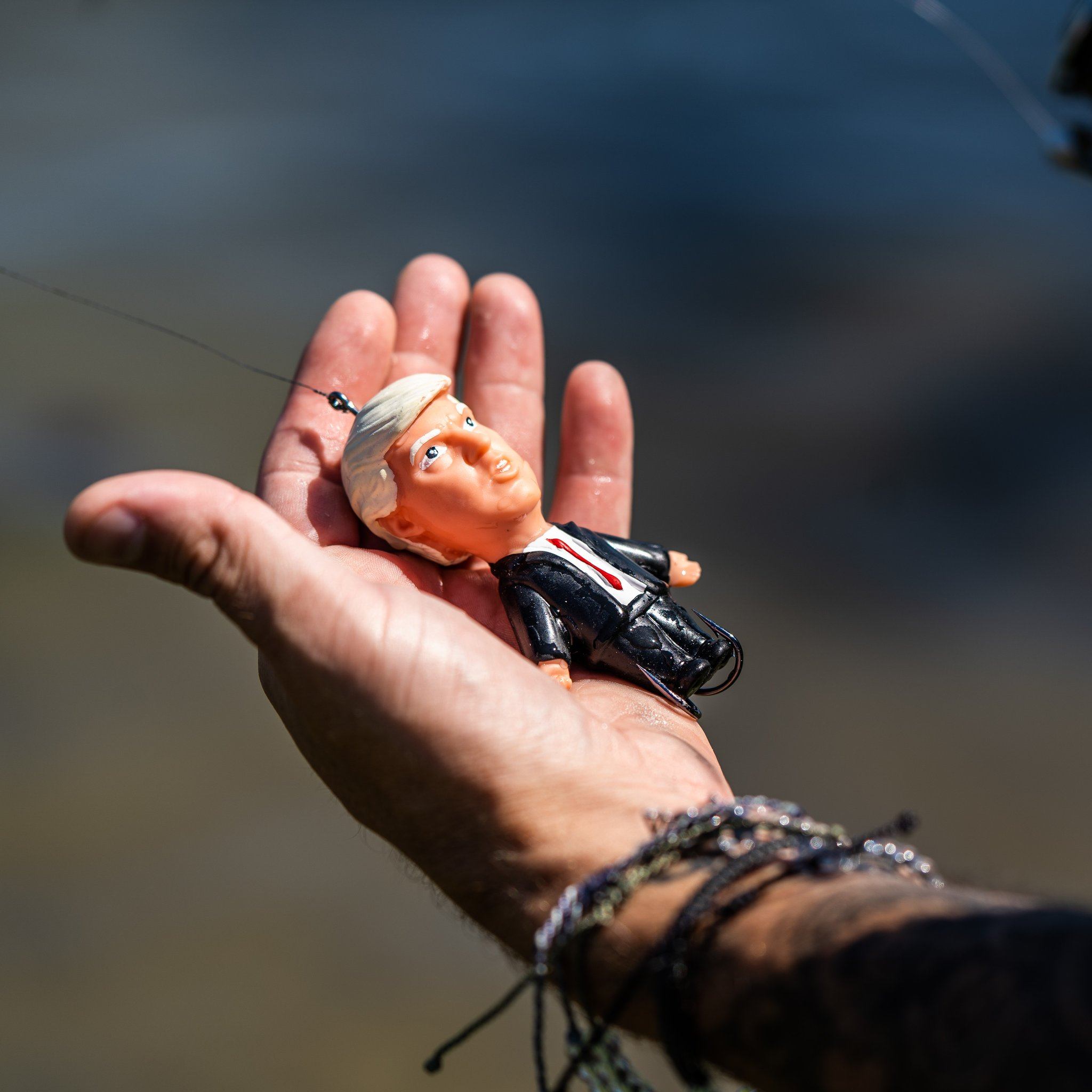 Fishing lure shaped like a person's head held in a hand against a blurred natural background