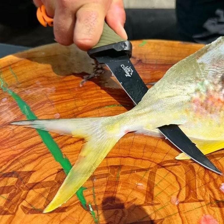 Person cutting a fish with a knife on a wooden cutting board